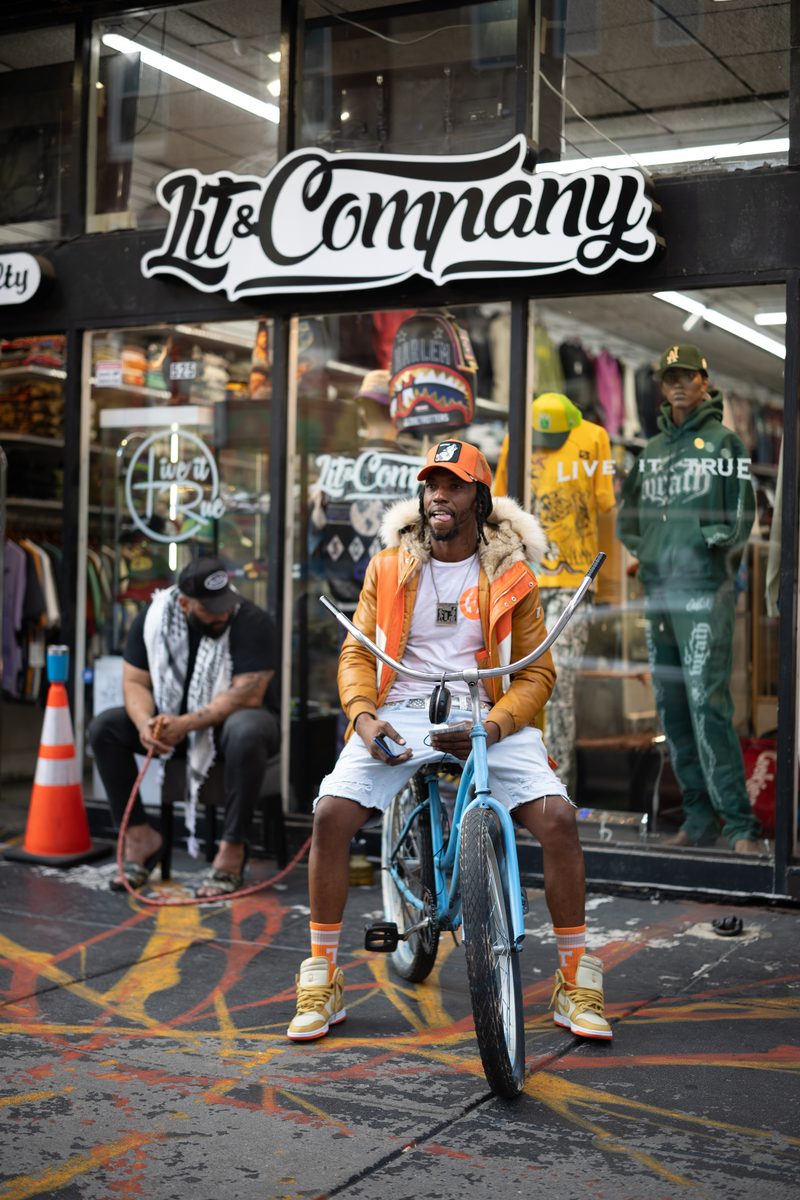A man in an orange jacket and matching sneakers sits on a blue bicycle outside the Lit & Company storefront on South Street.