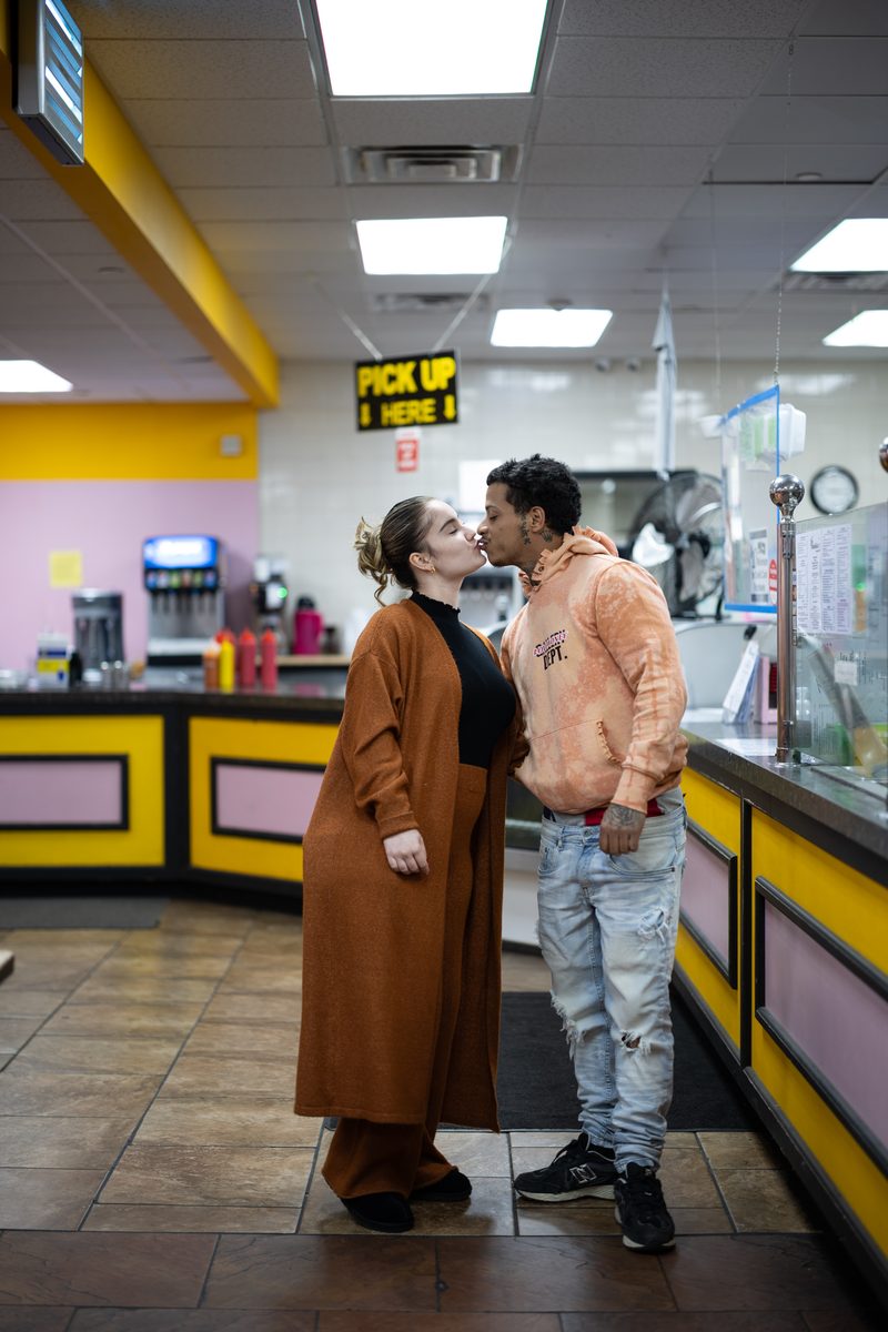 A couple kisses at the counter of a pink-and-yellow Ishkabibble's Philly cheesesteak spot on South Street.
