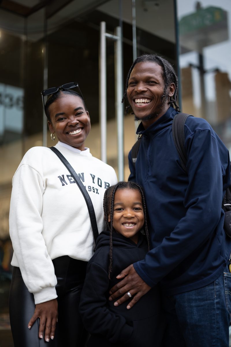 A smiling couple with their young son, who wears matching black, outside the storefront Status shoe store on South Street.