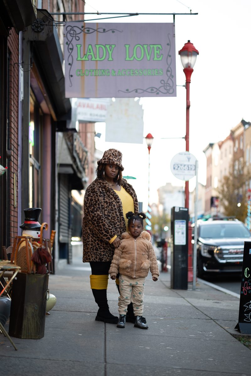 A woman in leopard print poses with her hand on the shoulder of her daughter next to a "Lady Love" sign on South Street.