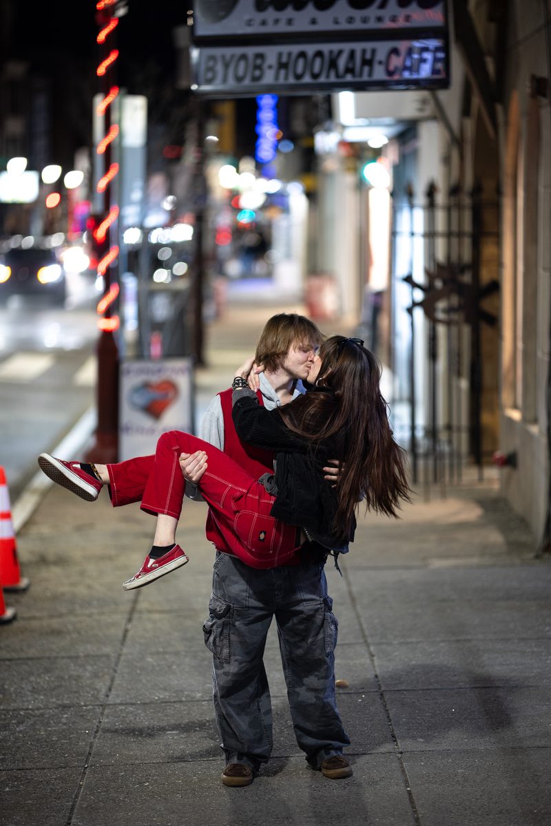 A young man in red pants lifts and kisses his partner on the sidewalk outside a South Street hookah lounge at night on Valentine's Day.
