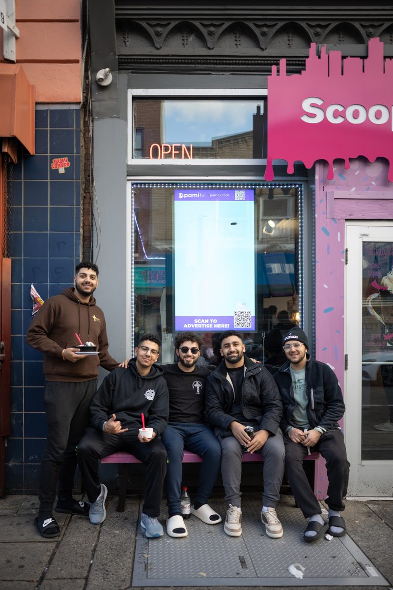 Five young men sit together on a bench outside the pink Scoop DeVille ice cream shop on South Street.