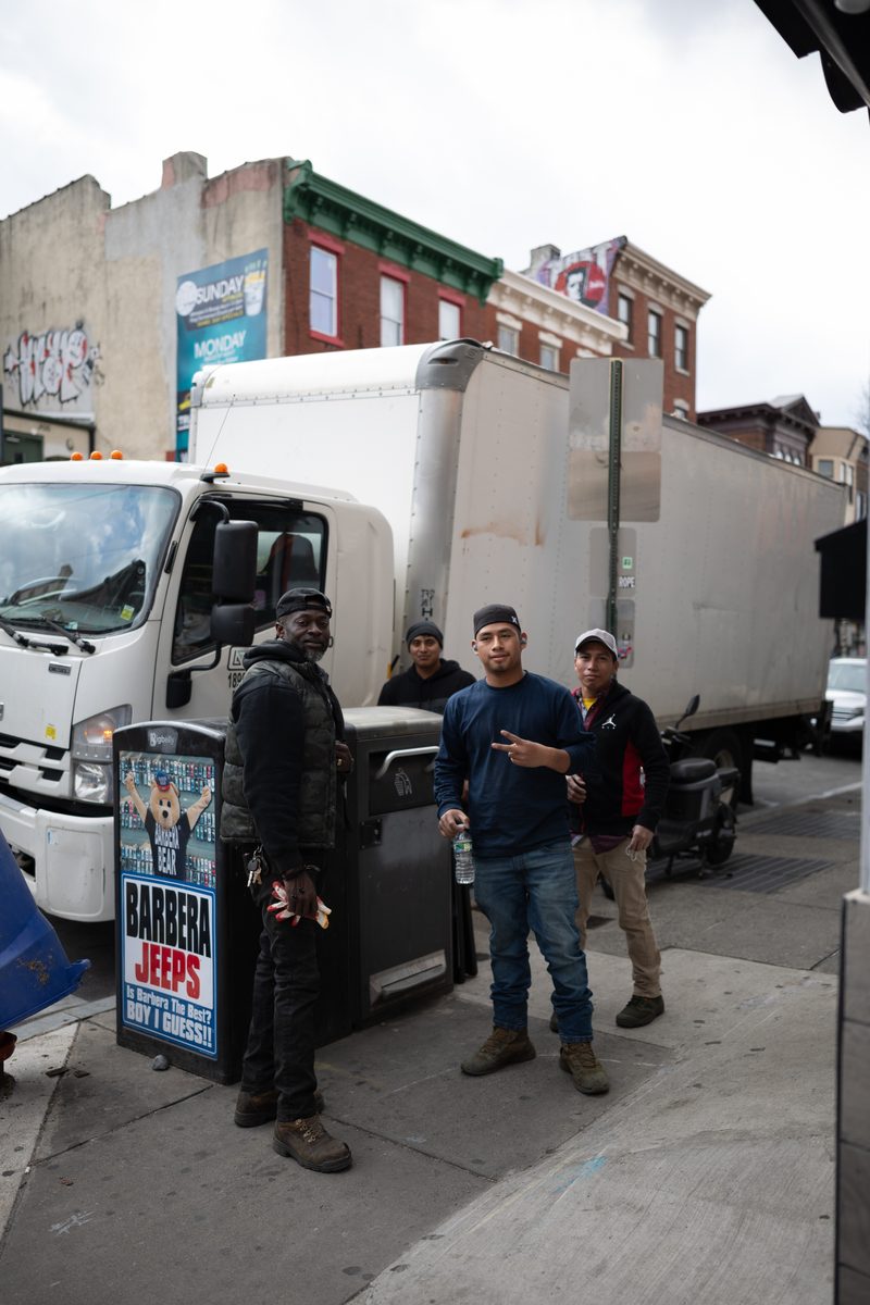 Four workers stand beside their box truck on South Street, one flashing a peace sign.
