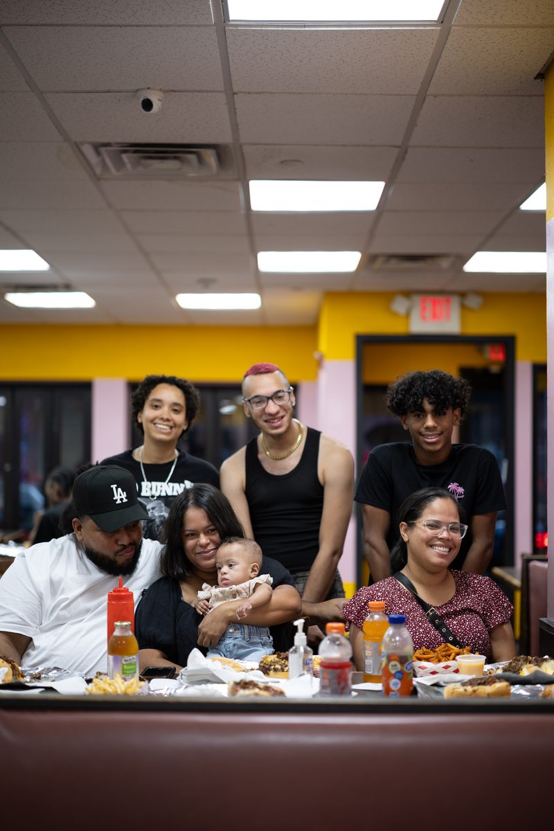 A large family crowds into a booth at Ishkabibble's on South Street, a baby in the center and food covering the table.