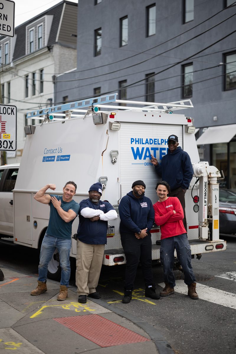 Five Philadelphia Water Department workers pose by their utility truck on South Street, one flexing their bicep.
