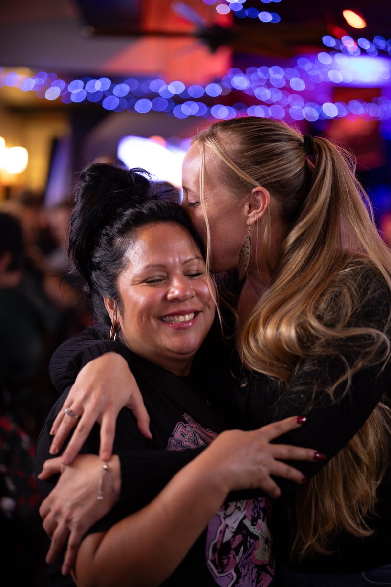 A young woman kisses her friend's head under blue and purple lights inside a South Street bar.