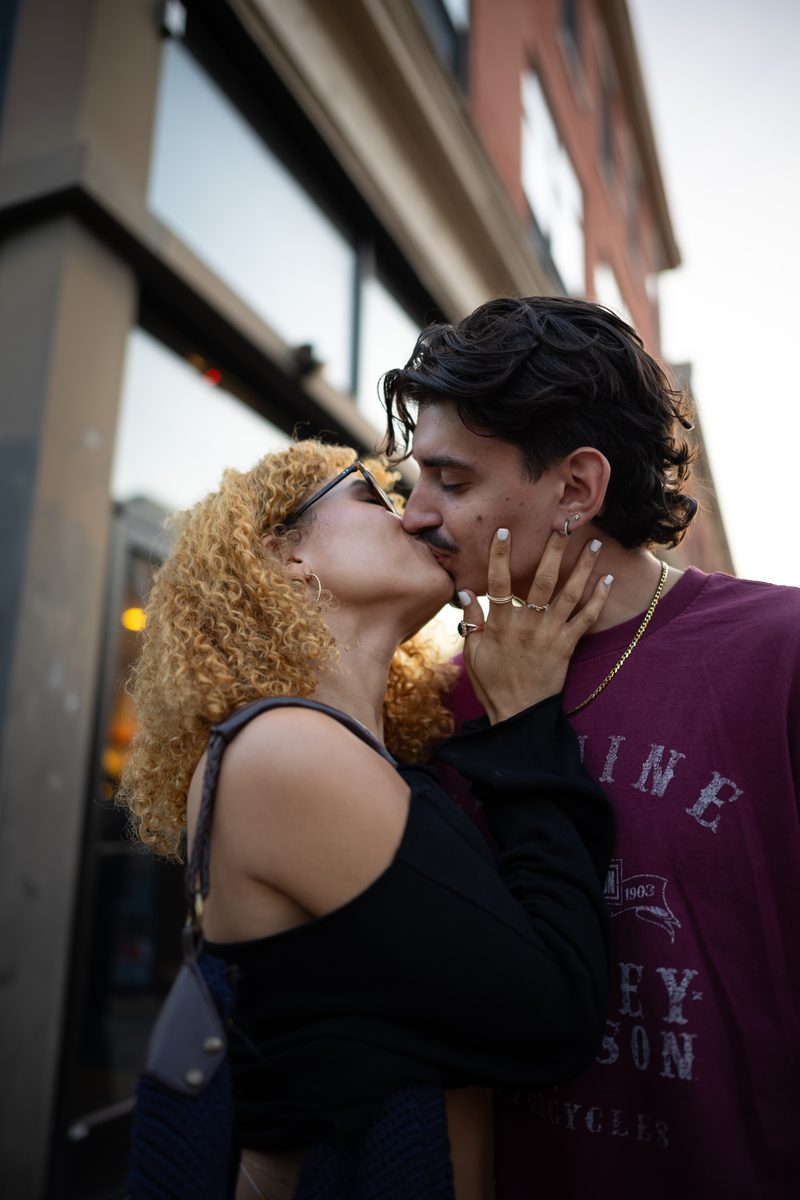 A woman with curly blonde hair kisses a man while holding his face outside a Starbucks coffee shop on South Street.