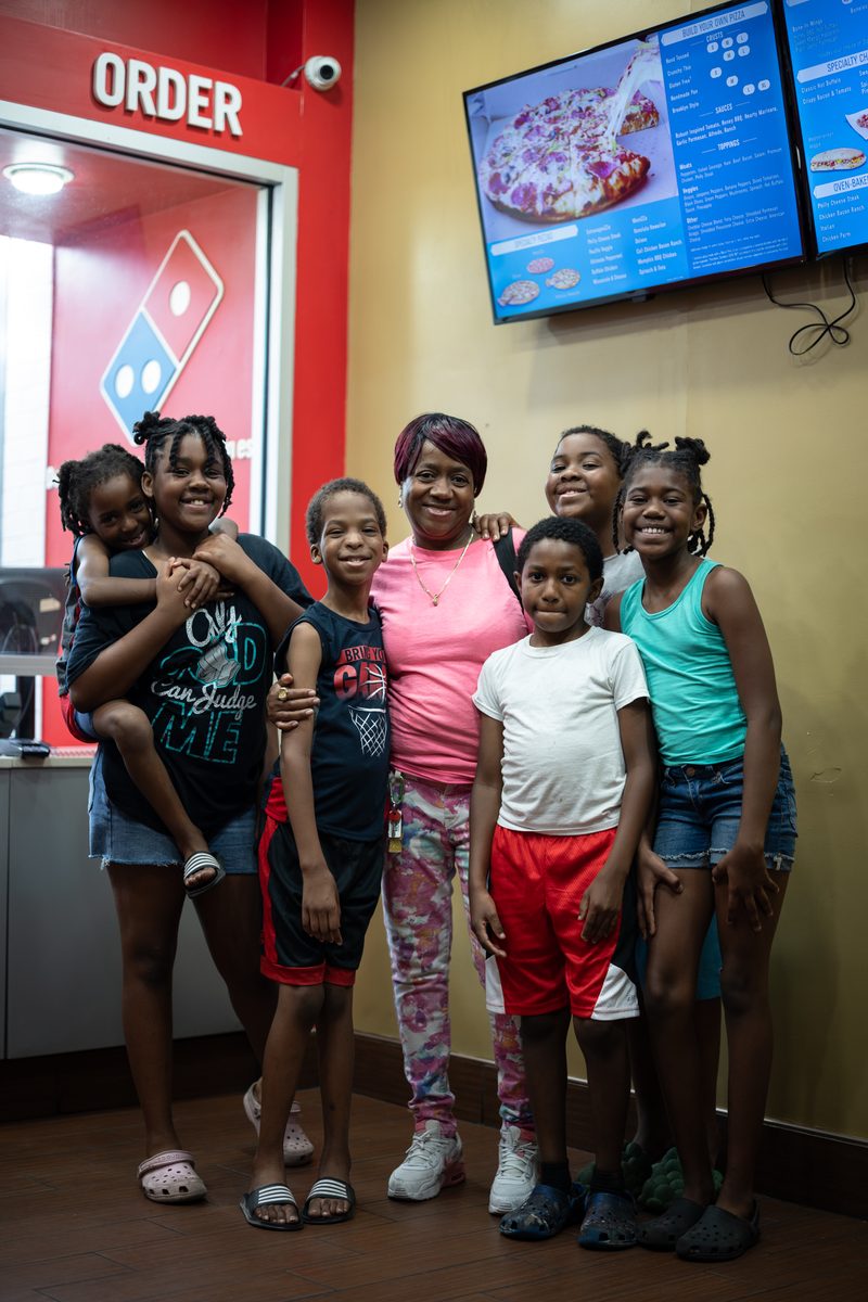 Six children and their grandmother smile together in a tight group inside a Domino's pizza shop on South Street.