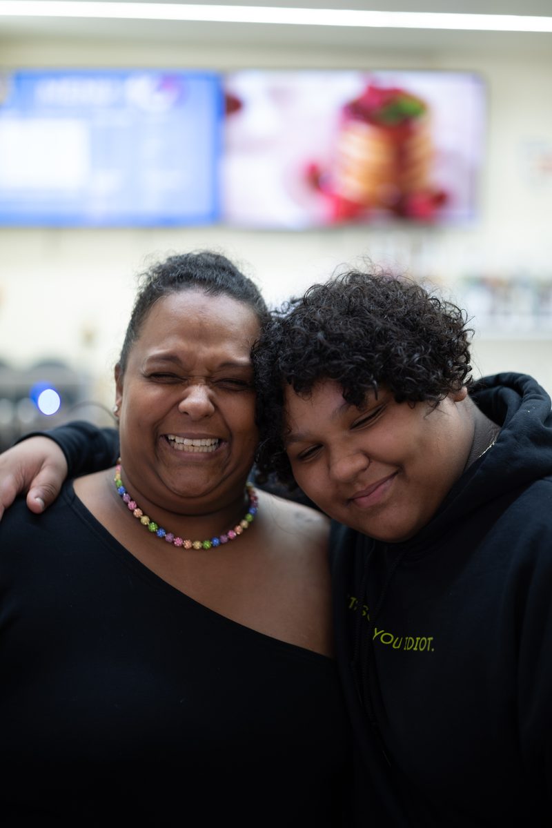 A mother in a beaded necklace and her curly-haired son squeeze their eyes shut laughing, cheek to cheek, inside an ice cream shop on South Street.