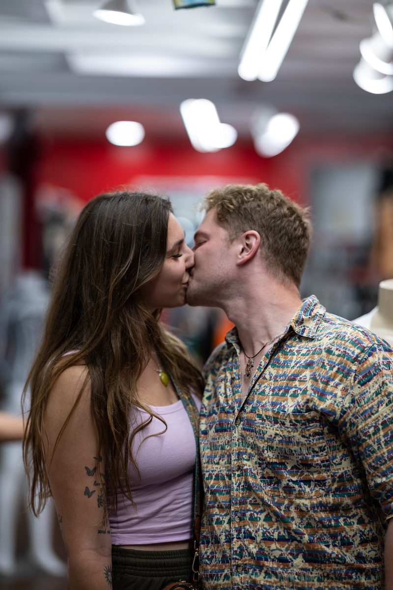 A couple kisses inside a South Street shop, she in a lavender tank top, he in a patterned button-up.