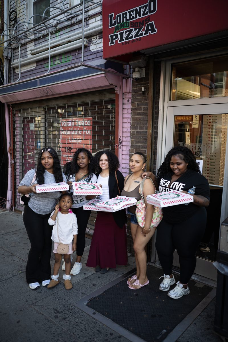 Five women and a little girl hold pizza boxes outside Lorenzo and Son's Pizza on South Street.