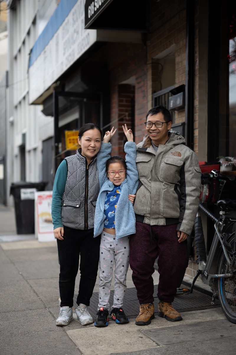 A family of three smiles on a South Street sidewalk outside Golden Empress Garden Chinese restaurant, the young daughter in the middle flashing peace signs.