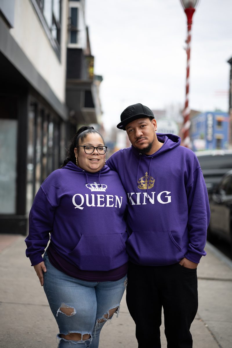 A couple in matching purple "Queen" and "King" hoodies stands together on South Street.