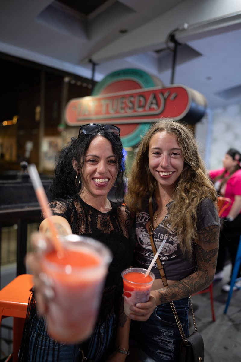Two friends hold frozen daiquiris up to the camera under the Fat Tuesday sign on South Street.