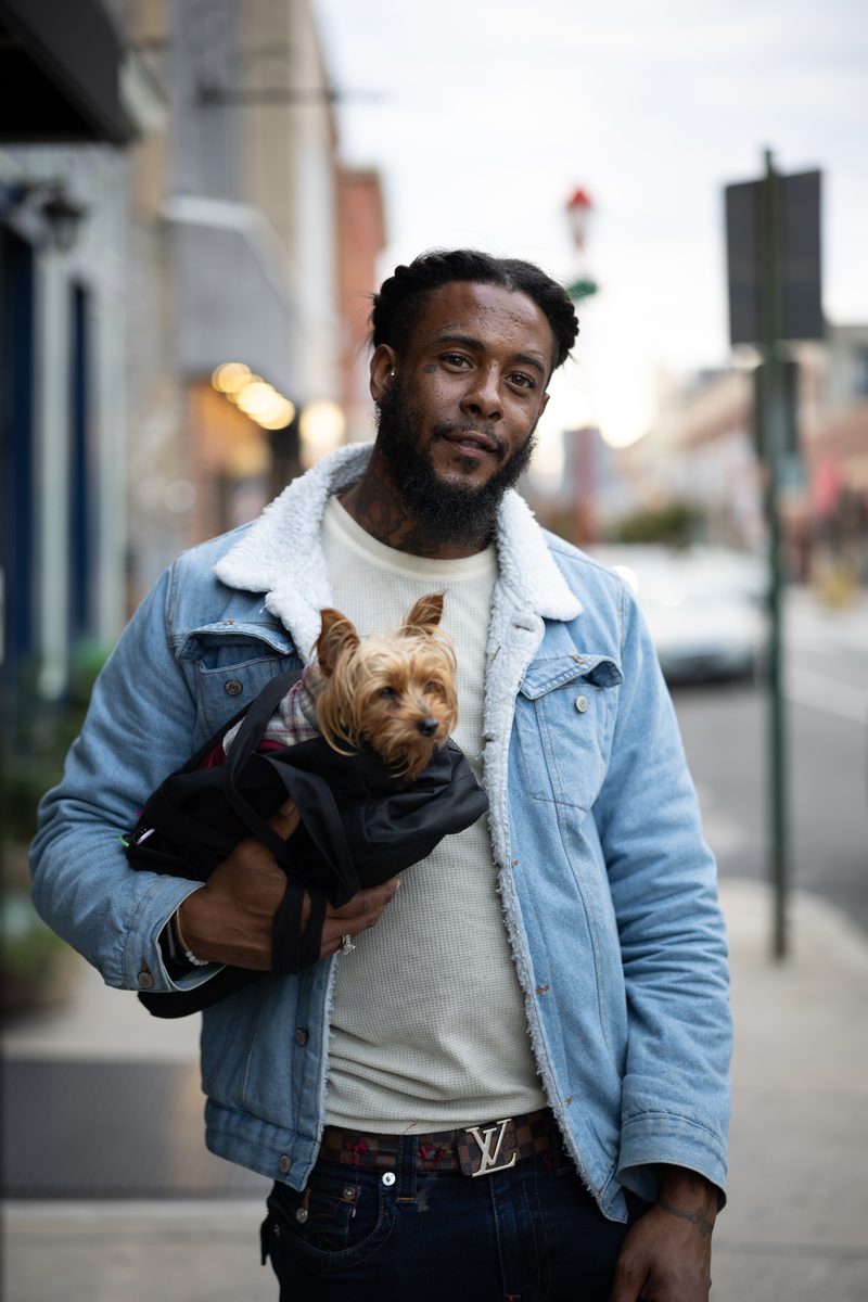 A man in a denim jacket and sherpa collar cradles his small Yorkie on a South Street sidewalk.