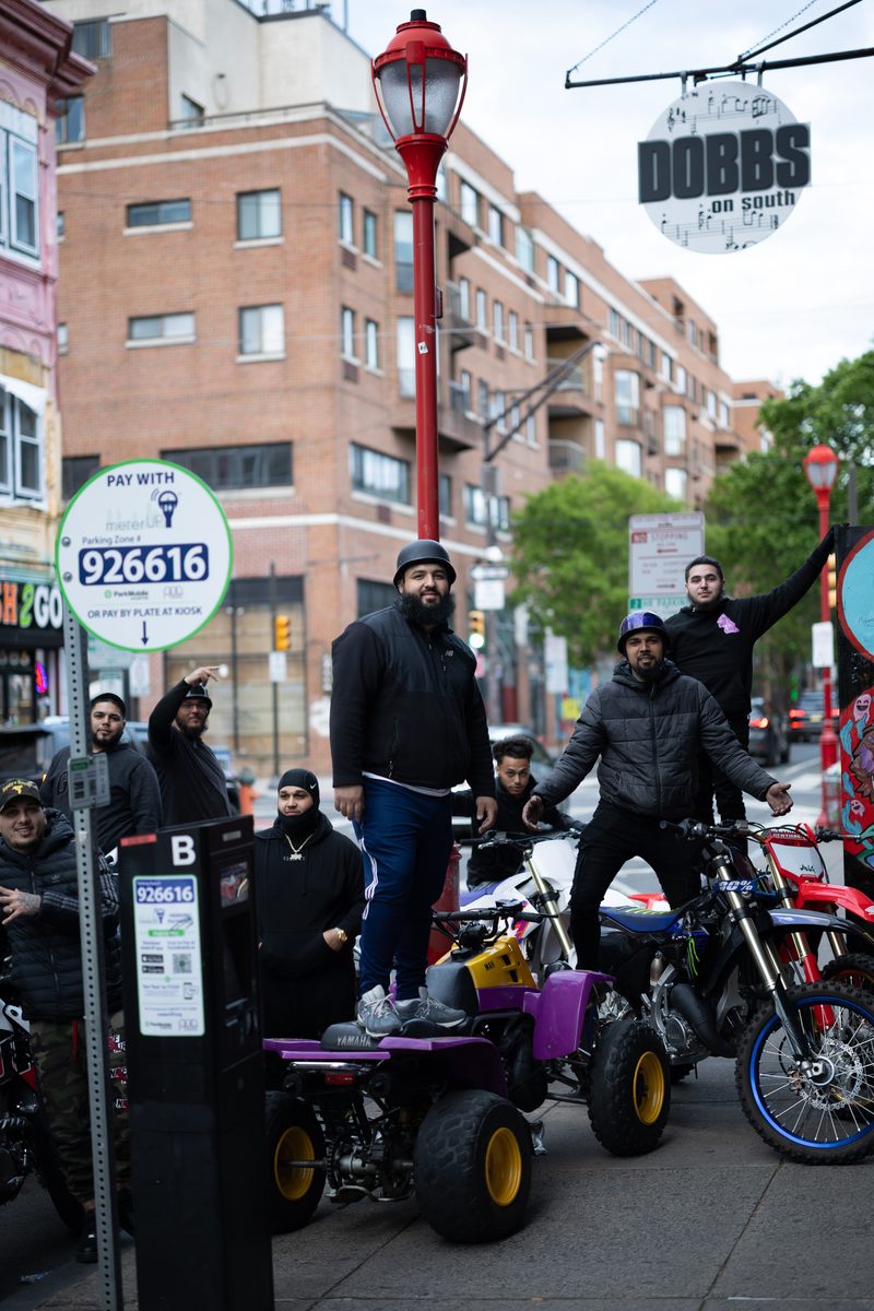 A group of young men on dirt bikes and a purple ATV pose in front of Dobbs on South Street.