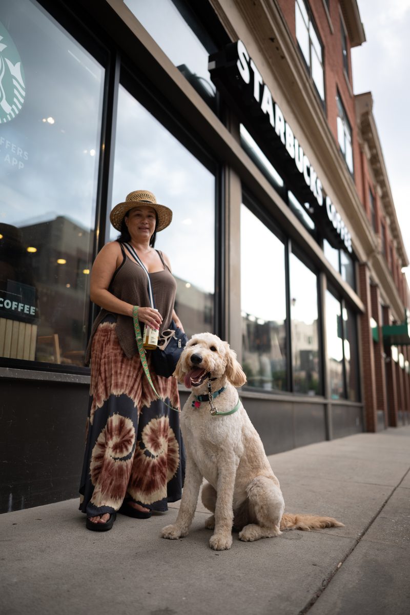 A woman in a straw hat and tie-dye skirt walks a golden doodle past the Starbucks on South Street.